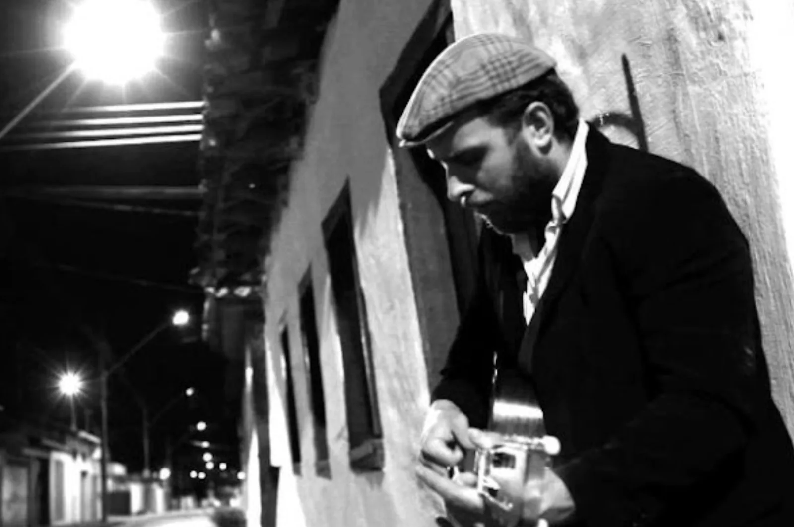 Big Creek Slim playing guitar beside an arched wall in a black-and-white photograph