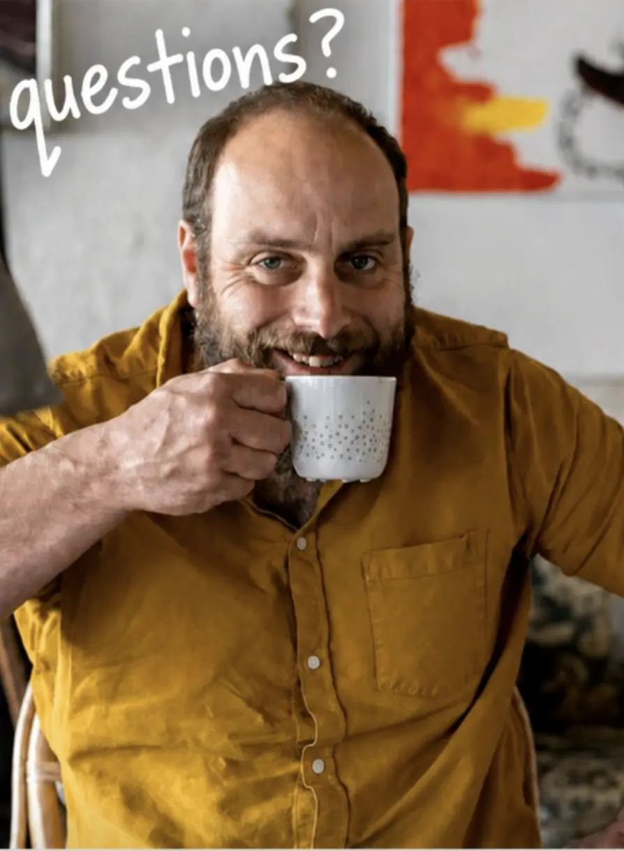 Big Creek Slim smiling over a cup of coffee with the handwritten word Questions